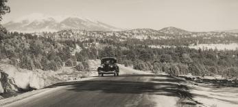 With the snowy San Francisco Peaks in the background, a motorist heads west on the stretch of Route 66 between Williams and Parks, likely in the 1930s or ’40s. | NORMAN G. WALLACE/ARIZONA HISTORICAL SOCIETY